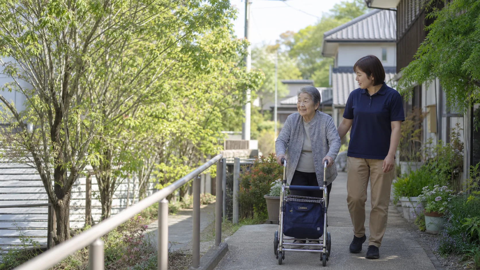 歩行器を使って庭沿いを歩く高齢の女性と職員